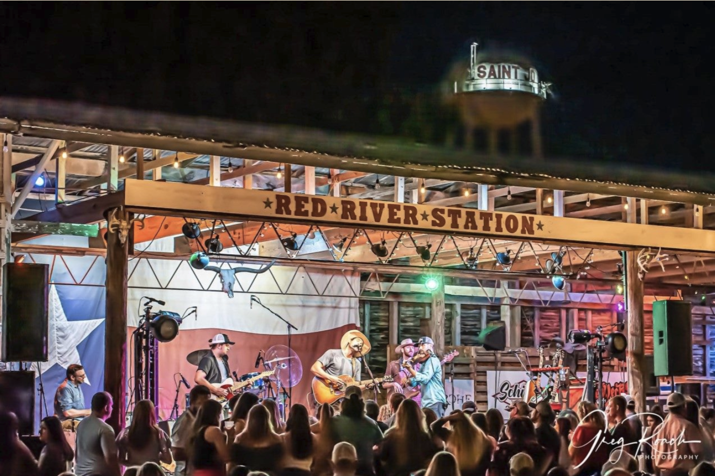 Band performing on the Red River Station stage under the Saint Jo water tower